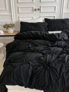 a bed with black comforter and pillows on it in front of a white door