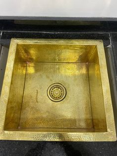 a gold square sink on a black counter top with a circular design in the center