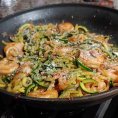 a skillet filled with shrimp and zucchini pasta on top of a stove