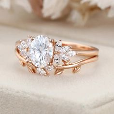 a rose gold ring with an oval cut diamond surrounded by smaller round diamonds and leaves