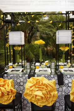 the table is set with black chairs and yellow flowers