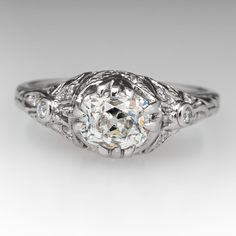 The ring is centered with one (1) old mine cut diamond four-split prong head. The ring features a pierced design and is accented with sixteen (16), bead/bezel set, round brilliant cut diamonds. Engraved wheat motifs accent the shank. The ring measures 8.0mm at the top, rises 8.0mm above the finger, tapering to 1.8mm wide and 1.0mm thick at the base of the shank. Platinum Cluster Ring With Diamond Cut, Heirloom Cushion Cut White Gold Diamond Ring, Heirloom Cushion Cut Diamond White Ring, Heirloom Platinum Diamond Ring With Classic Cut, Heirloom Ring With Center Stone In Classic Cut, Timeless Classic Cut Diamond Ring With Single Cut Diamonds, Heirloom Ring With Center Stone And Classic Cut, Timeless Diamond Ring With Single Cut Diamonds, Timeless Diamond Ring With Single Cut