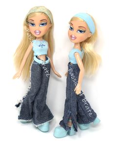 two dolls are standing next to each other on a white surface, one is wearing blue jeans and the other has blonde hair