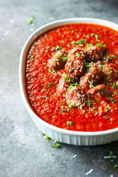 a white bowl filled with meatballs covered in marinara sauce and garnished with parsley