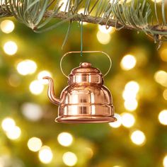 a copper teapot ornament hanging from a christmas tree with lights in the background