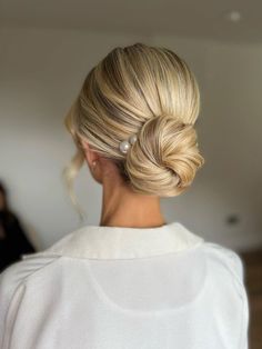 a woman with blonde hair styled into a low bun in a white sweater, looking off to the side