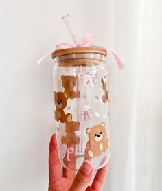 a hand holding a clear glass with brown bears on it and pink ribbon around the top