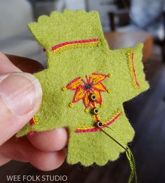 a hand holding a small green piece of felt with flowers and beads on the side