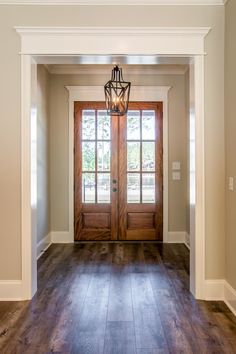 an empty entryway with two wooden doors and a light fixture hanging from the ceiling