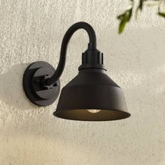 an outdoor light mounted on the side of a white wall with a plant in front of it