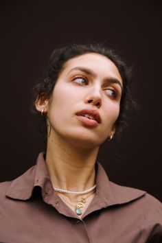 a woman with her eyes closed wearing a brown shirt and pearl necklace, looking up at the sky