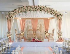 a wedding ceremony setup with white and pink flowers on the head table, gold chairs and draping