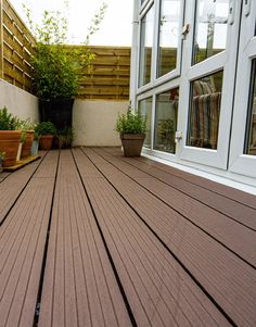 a wooden deck with potted plants on the side and windows to the other side