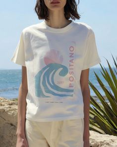 Seize the surf in our Positano 1980 Tee. For the girl who makes waves both on the beach and off, this is your summer statement tee. Unisex soft cotton crew neck t-shirt featuring a Positano Italy Surf Camp graphic printed on the front. Fabrics: 100% cotton, 6 oz Made in: LA Retro White Top For Beach, Beachy White Cotton Tops, White Cotton Beachy Tops, Beachy White Short Sleeve Tops, White Short Sleeve Beachy Tops, White Relaxed Fit Top For Surfing, White Crew Neck T-shirt For Surfing, White Graphic Tee For Surfing, White Screen Print T-shirt For Beach Season