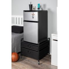 a black and silver refrigerator sitting on top of two drawers in a bedroom next to a bed