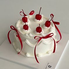 a cake with white frosting and cherries on top, tied in red ribbon