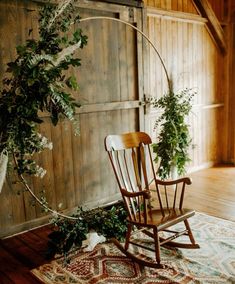 a rocking chair sitting on top of a rug next to a wooden wall with plants growing out of it