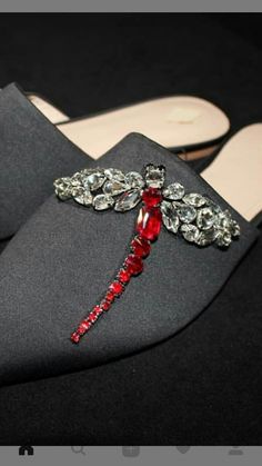 a pair of black shoes with red and clear jeweled dragonfly brooch on them