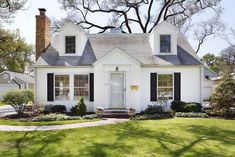 a white house with black shutters on the front door and windows in the middle