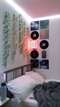 a bed sitting under a neon light next to a wall mounted with records and plants