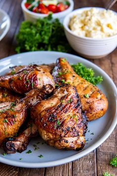 grilled chicken legs on a plate with vegetables and mashed potatoes in the background