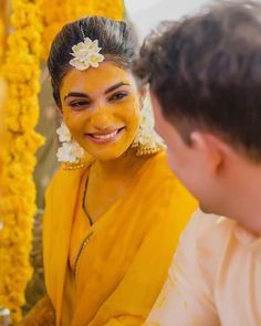 a woman with yellow paint on her face smiles at a man in front of flowers