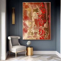 an abstract painting hangs on the wall next to a white chair and gold side table