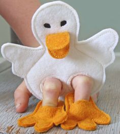 a white duck with yellow feet is sitting on the floor next to someone's hand