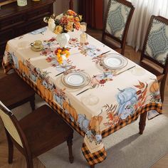 a dining room table set with place settings and flowers on the table cloth, in front of a window