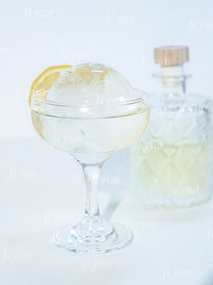 a glass filled with liquid next to a bottle on a white tablecloth covered surface