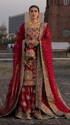 a woman in a red and gold bridal outfit standing on a brick floor with her hands on her hips