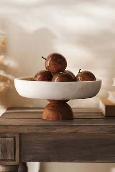 a white bowl filled with apples sitting on top of a wooden table next to books