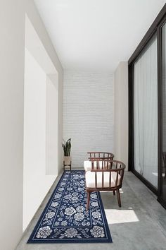 a long hallway with a chair and rug on the floor next to glass doors that lead into another room