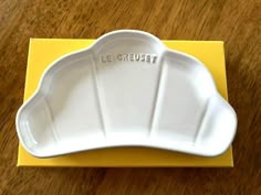 a white plate sitting on top of a yellow box with the word le crueet written in it