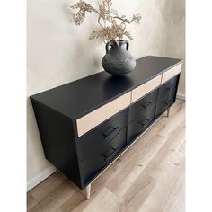 a black vase sitting on top of a dresser next to a white wall and wooden floor