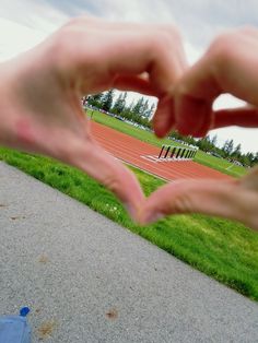 someone making a heart shape with their hands on the ground in front of a track