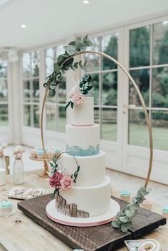 a three tiered wedding cake sitting on top of a wooden table next to donuts