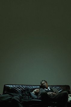 a man laying on top of a black couch next to a woman in a dark room