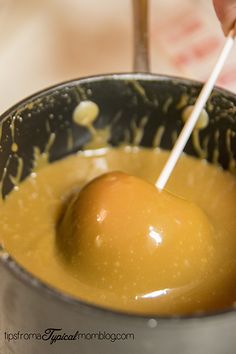 a person is dipping an apple into some liquid in a metal bowl on a table