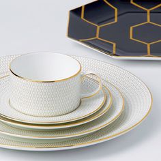 a stack of white and gold dinnerware with hexagonal plates in the background