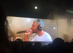 a man with headphones on singing into a microphone in front of a large screen