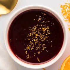 a white bowl filled with liquid next to an orange slice and spoon on top of a table