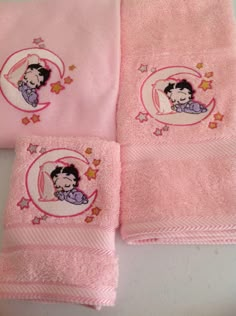 three pink towels with embroidered images of children's faces and stars on them, sitting next to each other