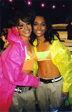 two women standing next to each other in front of a stage with bright colored lights