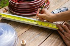 a person holding a pencil and measuring the length of a piece of plastic tubing