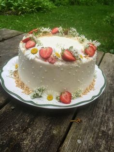 a white cake with strawberries and daisies on top sitting on a wooden table