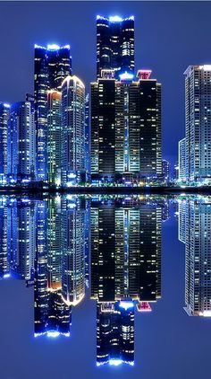 the city is lit up at night and reflecting in the water