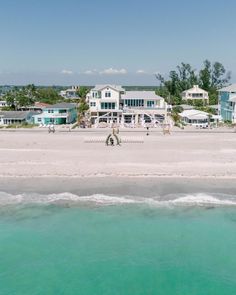 an aerial view of the beach with houses in the background and clear blue water at the foreground