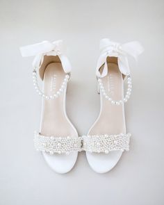 a pair of white shoes with pearls and bows on the heel, all tied together