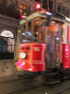 a red and white train traveling down tracks next to a tall building at night time